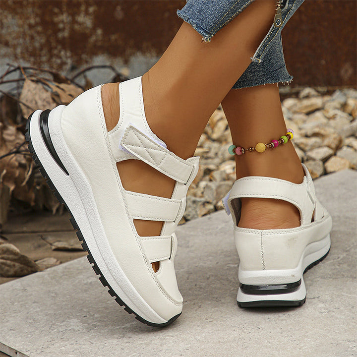 Woman wearing stylish white sneakers while standing on a plain background.