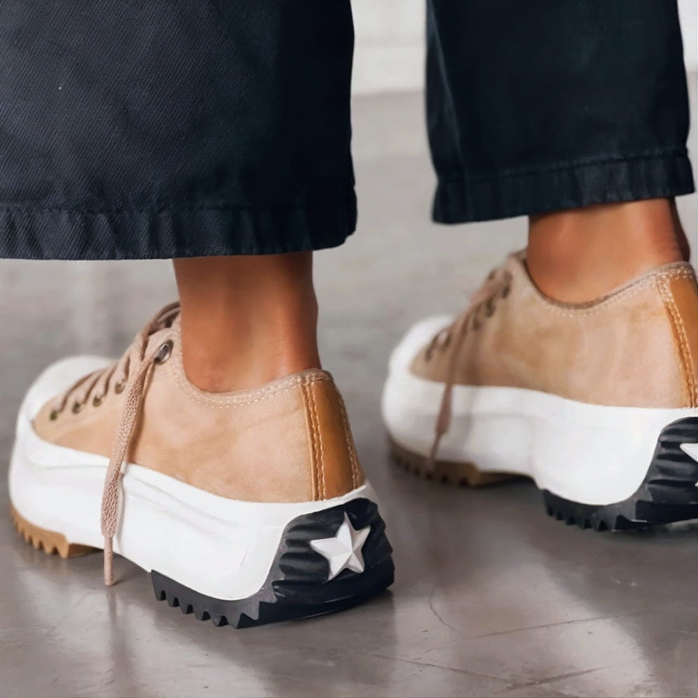 Female feet in cushioned everyday sneakers with a plain studio background.
