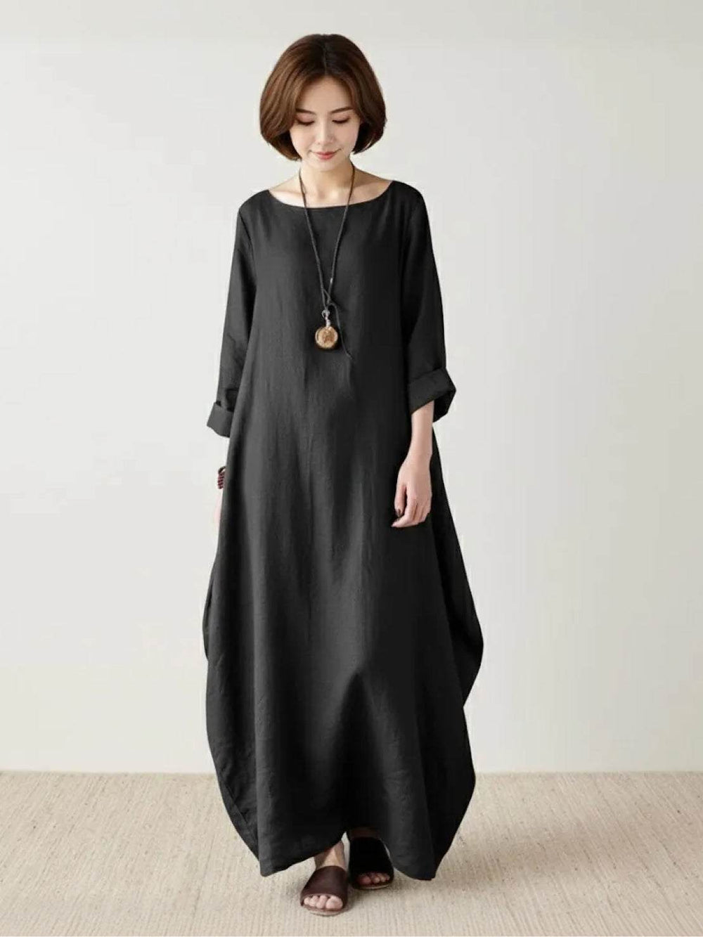 Woman posing in a flowing full-length dress with relaxed styling on a plain background.