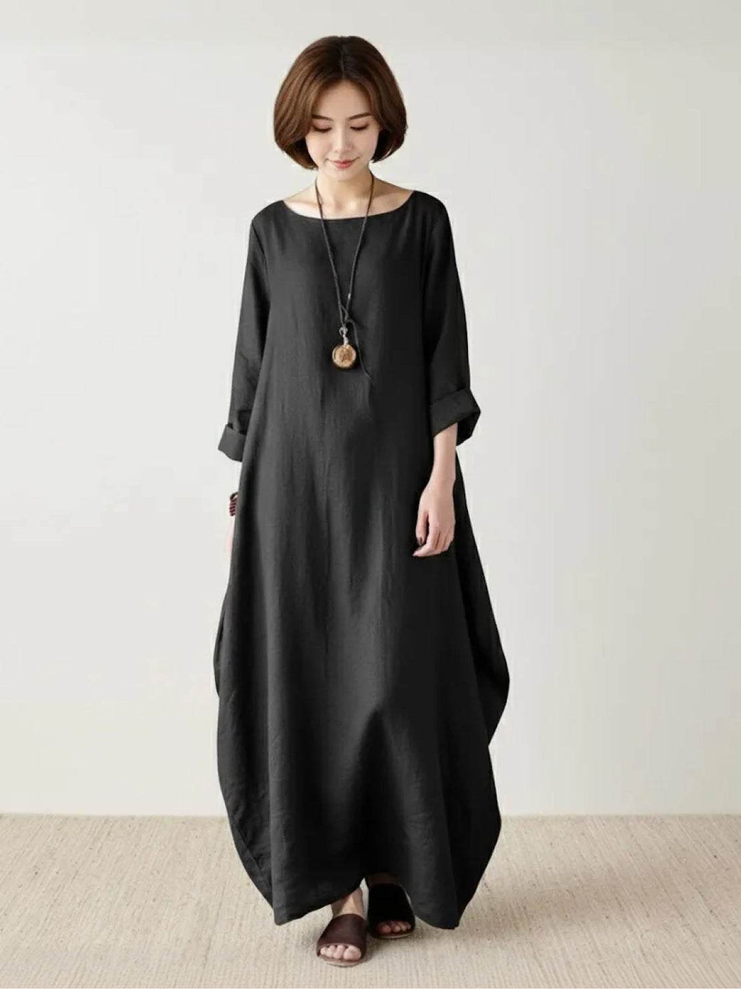 Woman posing in a flowing full-length dress with relaxed styling on a plain background.