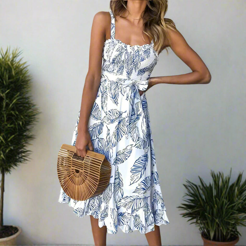 Woman posing in a printed midi dress featuring a tie waist and flowing skirt on a plain background.