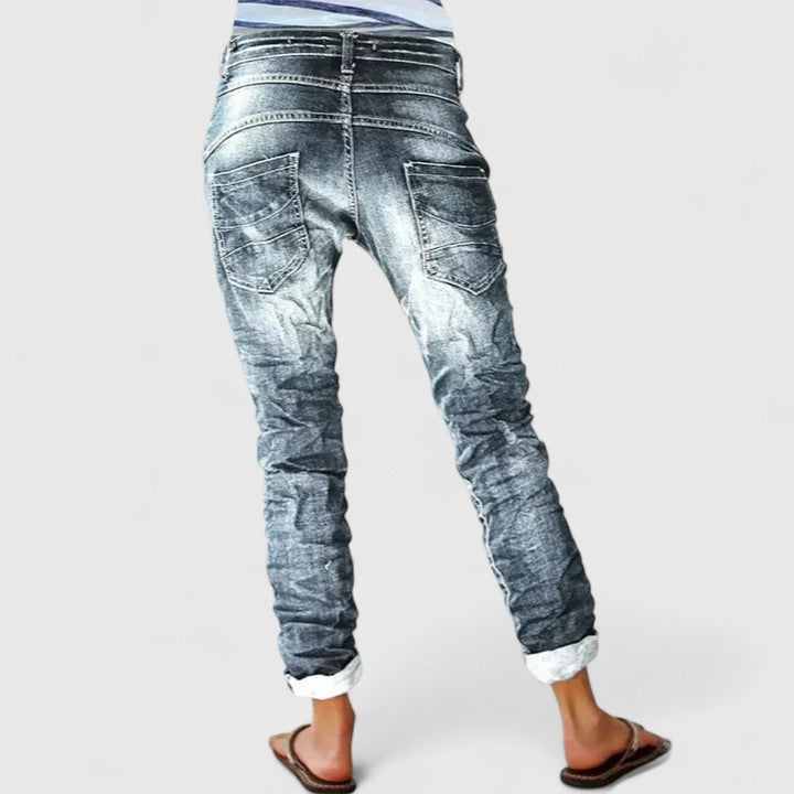 Casual tapered jeans with heavy distressed details on a plain background.