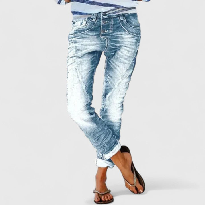 Women’s distressed tapered jeans on a plain background.
