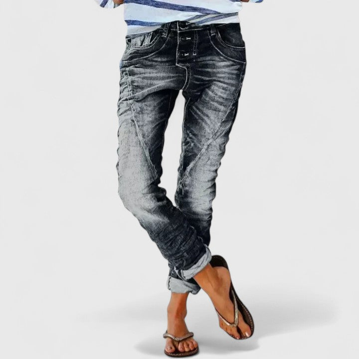 Distressed tapered jeans in grey wash on a plain background.