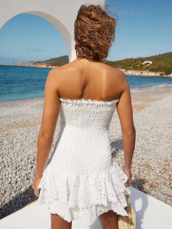  Female model displaying a flowy tiered dress with soft detailing against a plain background.