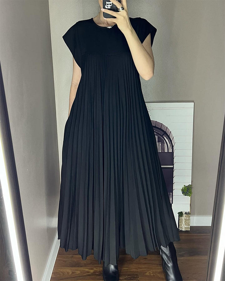Female model posing in a sleeveless pleated maxi dress on a plain backdrop.