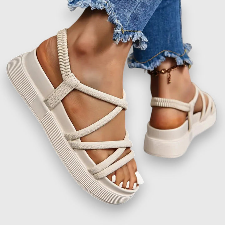 Female model wearing stylish women’s sandals on a plain studio background.