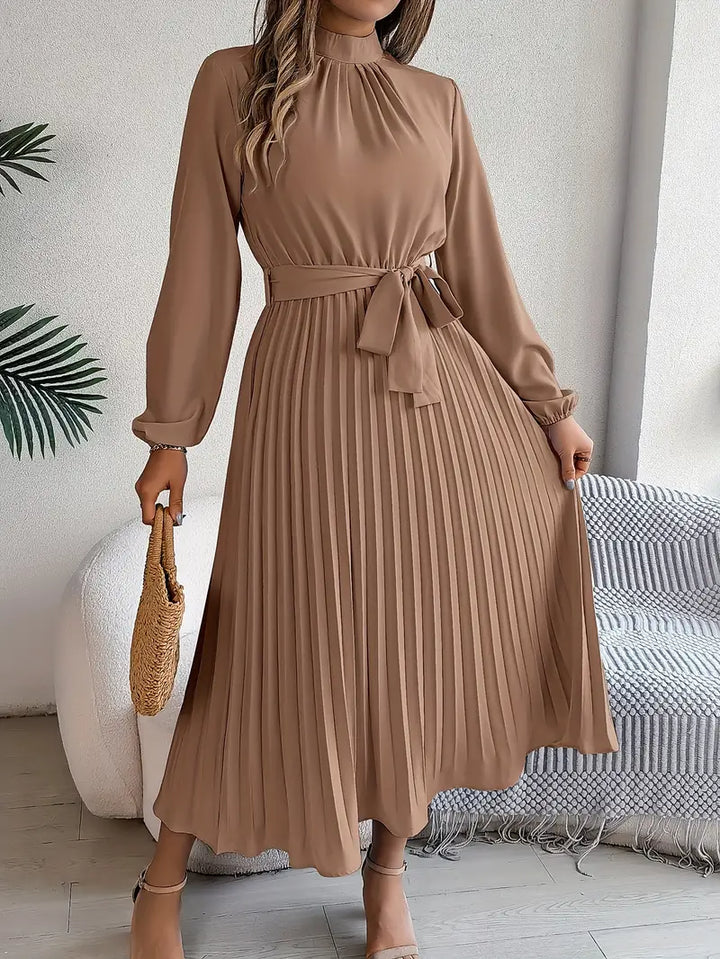 Woman in a winter-ready long sleeve dress with pleated details on a plain background.