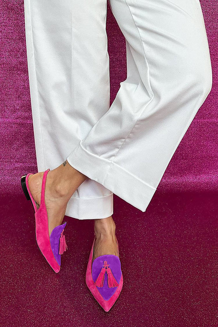 Female model showcasing fringe detail flat shoes on a plain background.