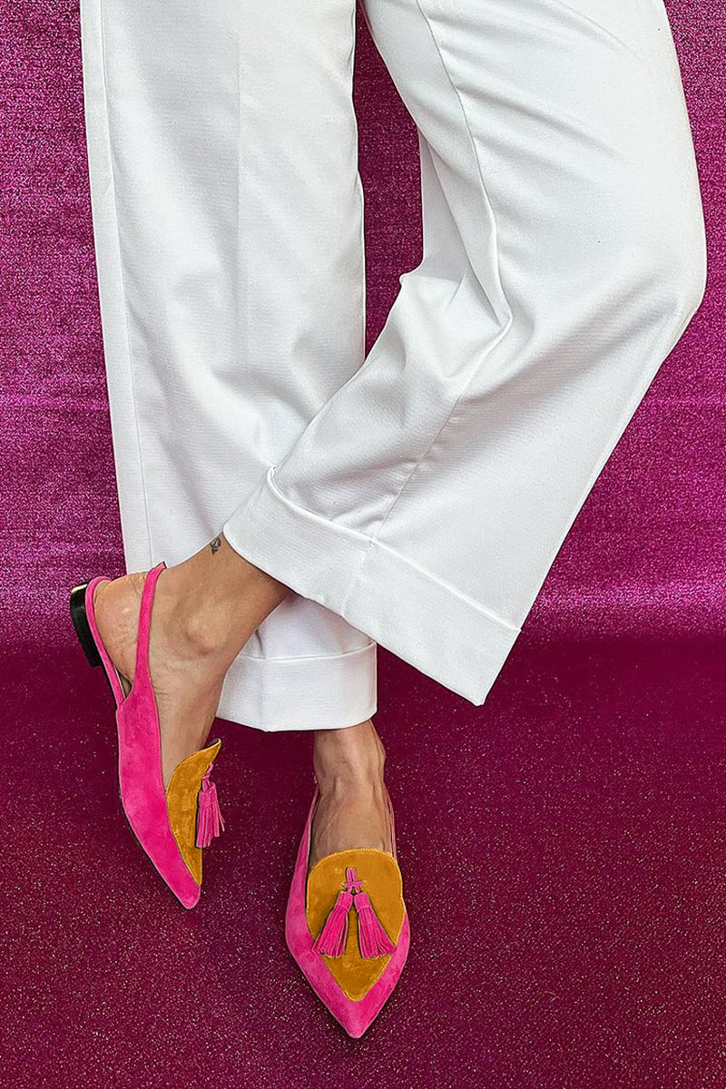 Woman styling colourful fringe flat shoes with a casual outfit on a plain background.