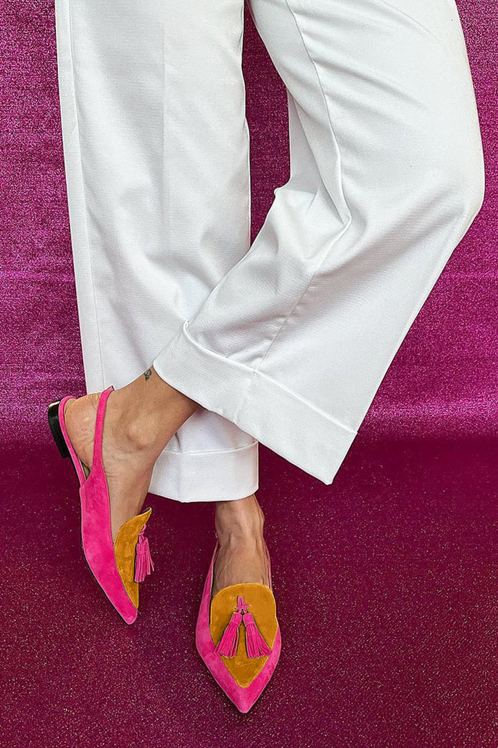 Woman styling colourful fringe flat shoes with a casual outfit on a plain background.