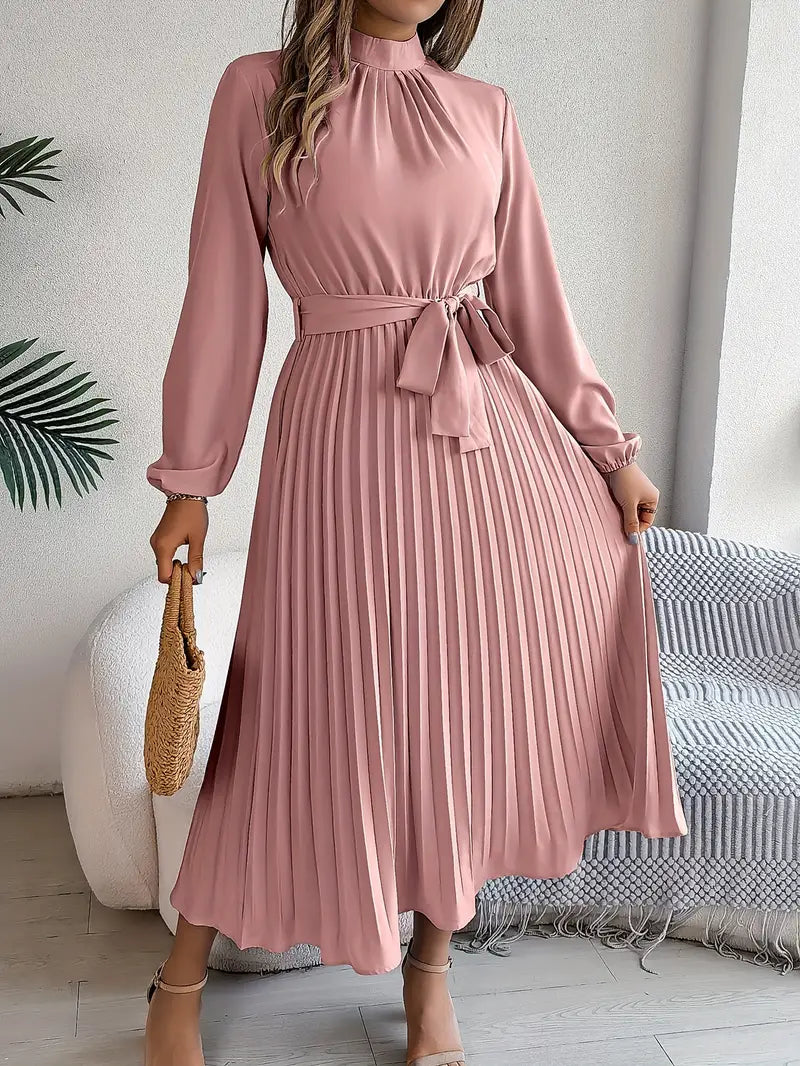 Female model wearing a flowing pleated dress with waist tie on a plain background.