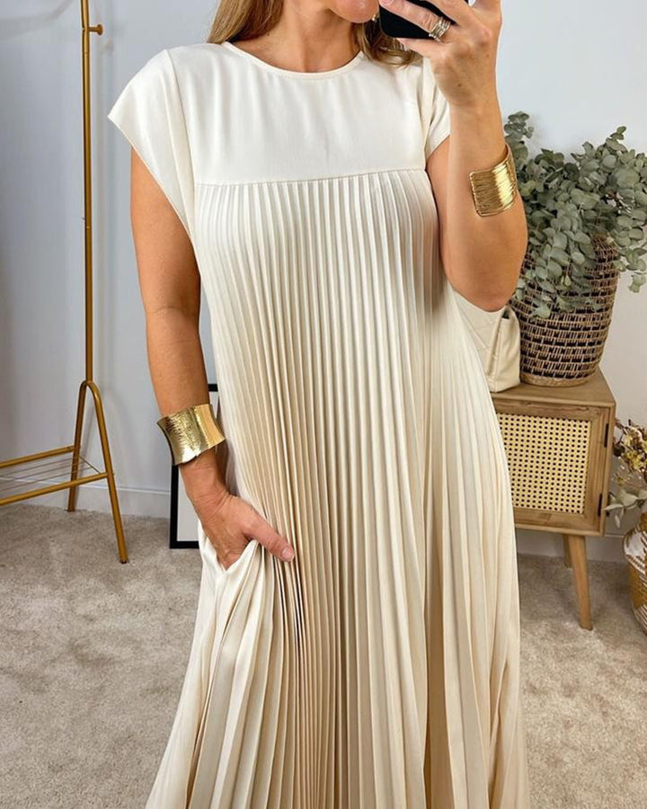 Woman wearing a flowy pleated maxi dress against a plain background.