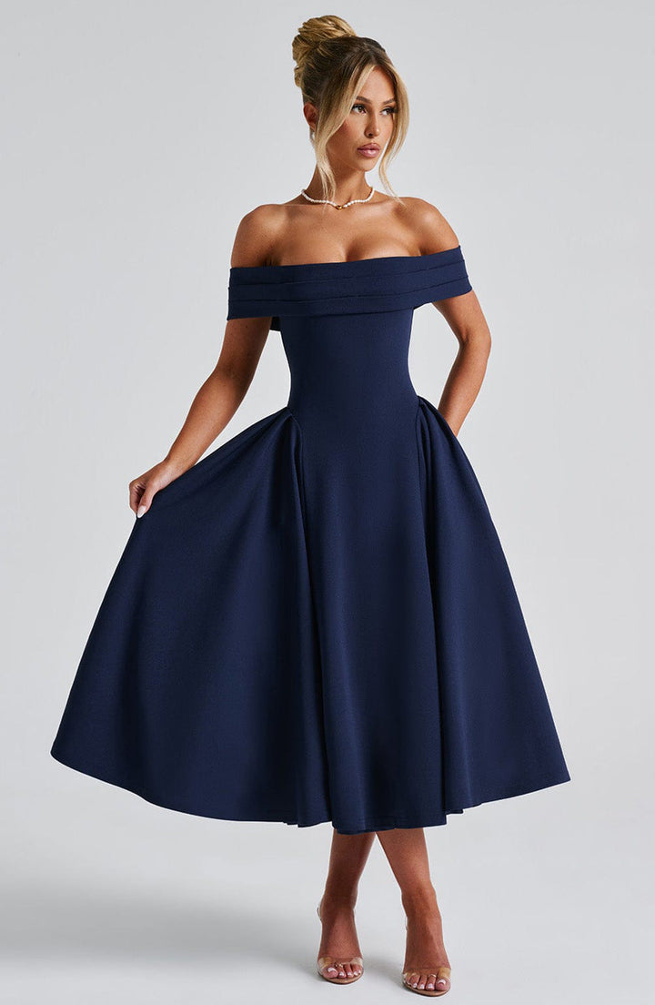Woman posing in an elegant formal midi dress against a plain background.