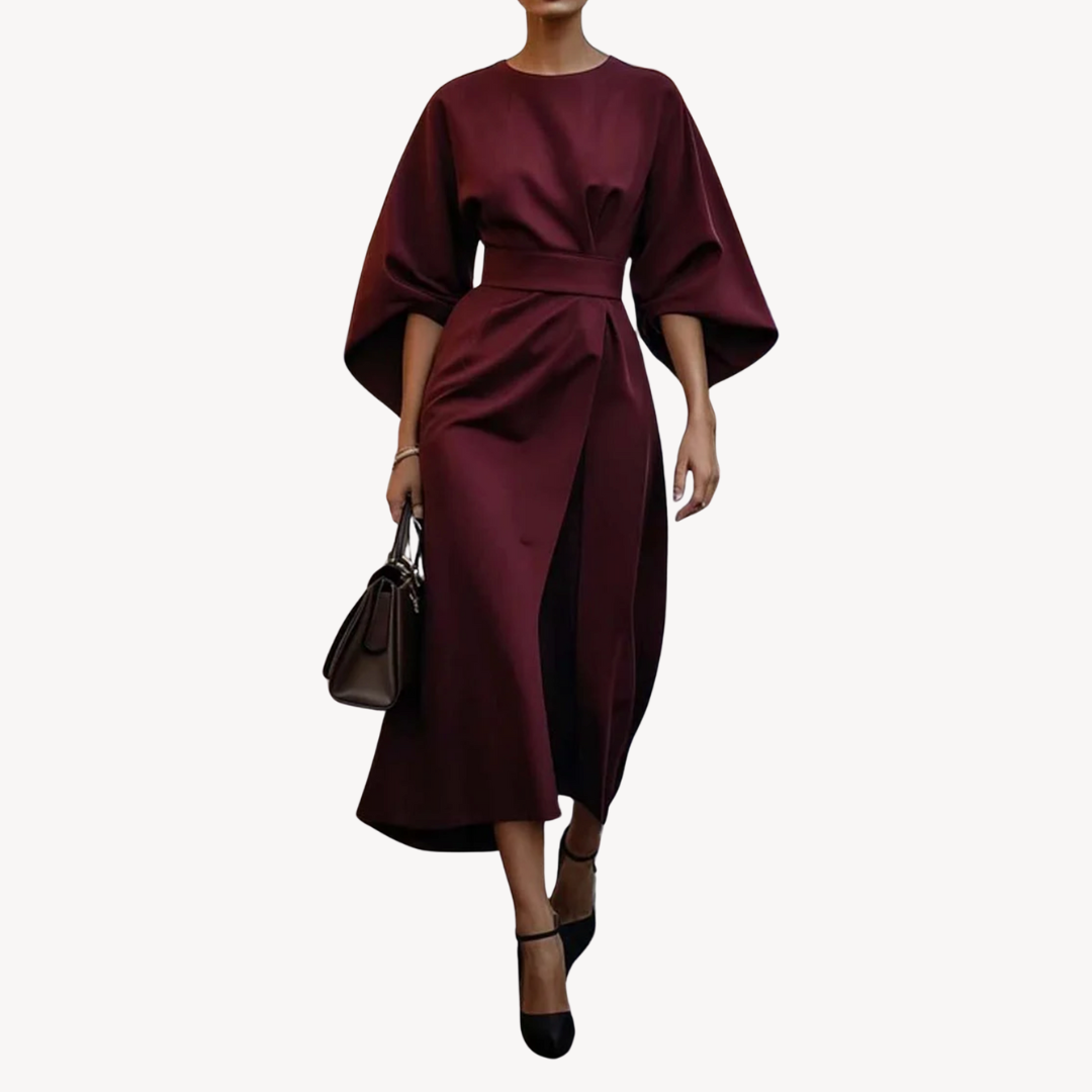 Woman showcasing a belted midi dress with flowing sleeves against a plain background.
