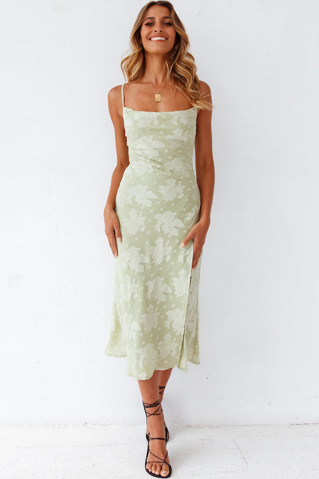 Woman wearing a floral cowl neck slip midi dress with high slit on a plain background.