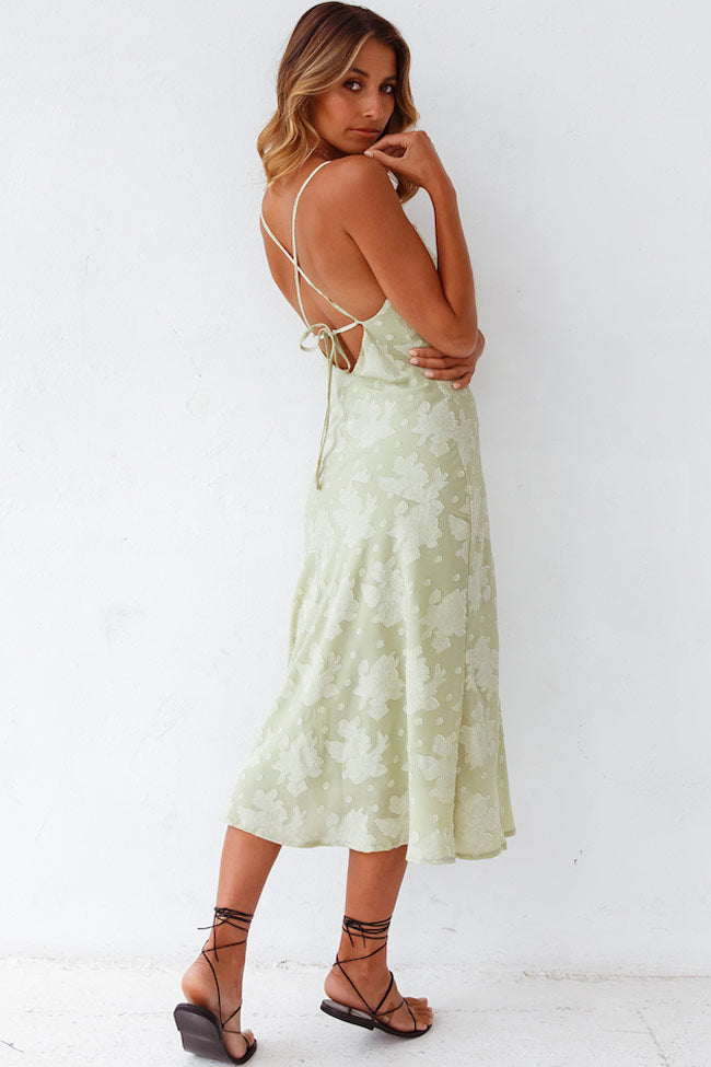 Female wearing an elegant floral midi dress with smooth fabric and high slit on a plain background