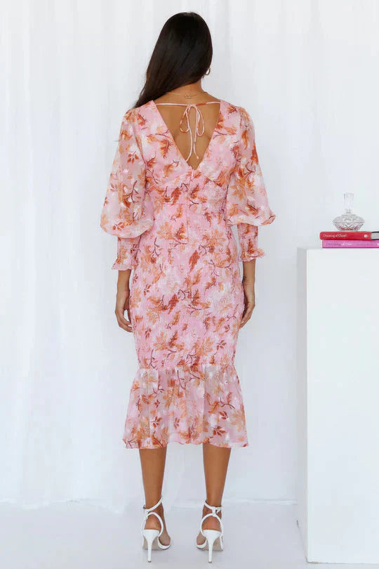 Woman in a breezy flower print dress against a plain background, back view