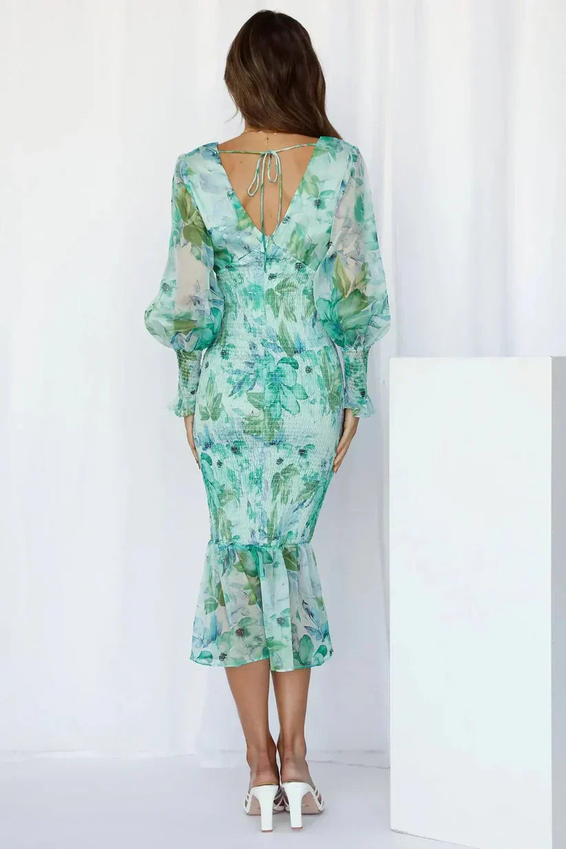 Woman posing in a vibrant flower dress with a plain background, back view