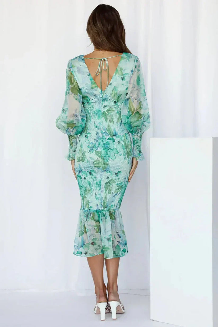 Woman posing in a vibrant flower dress with a plain background, back view