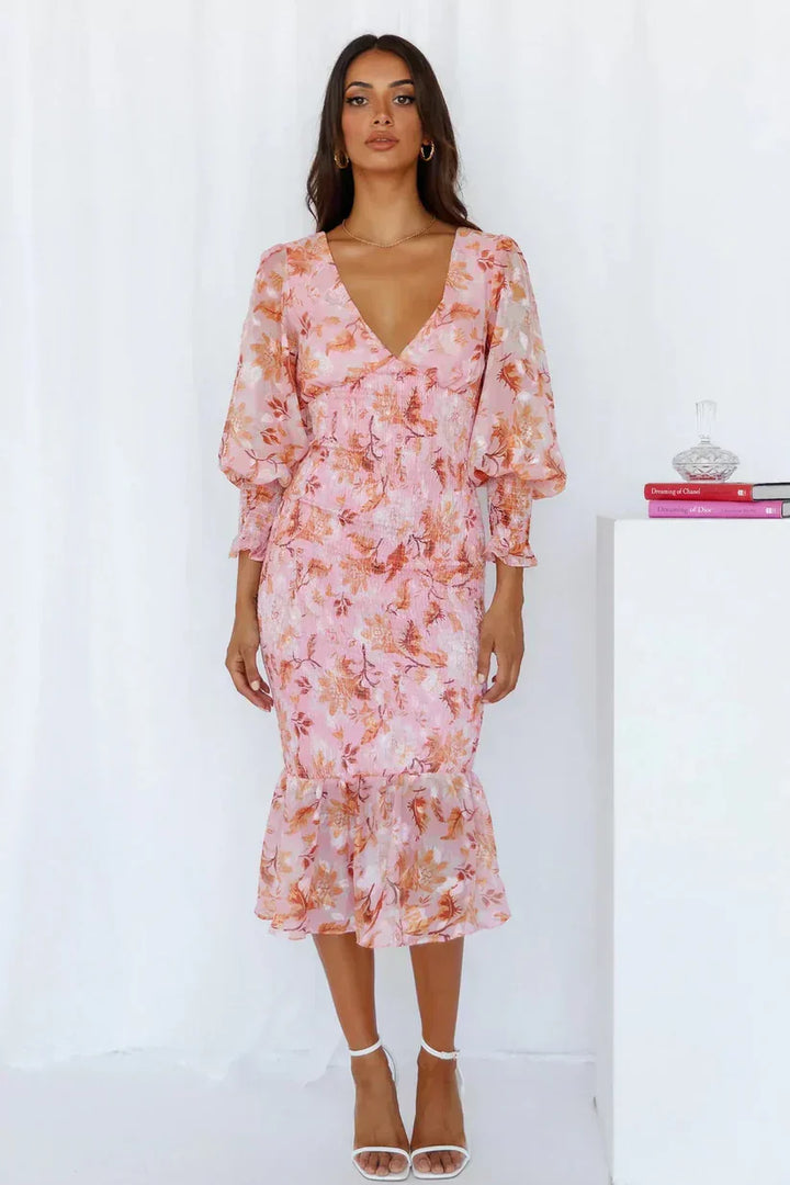 Female model wearing a bright floral dress on a clean background.