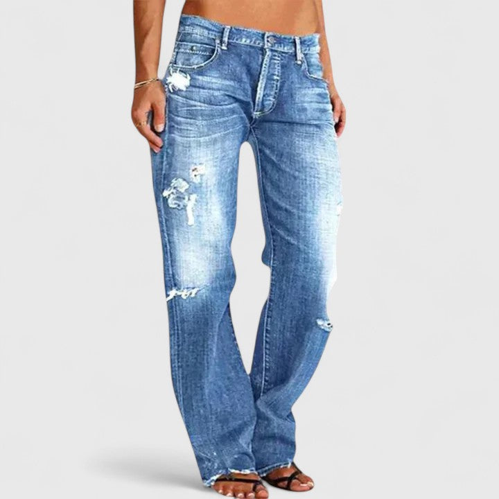 Female model wearing retro-inspired flare jeans with a relaxed stance on a plain background.