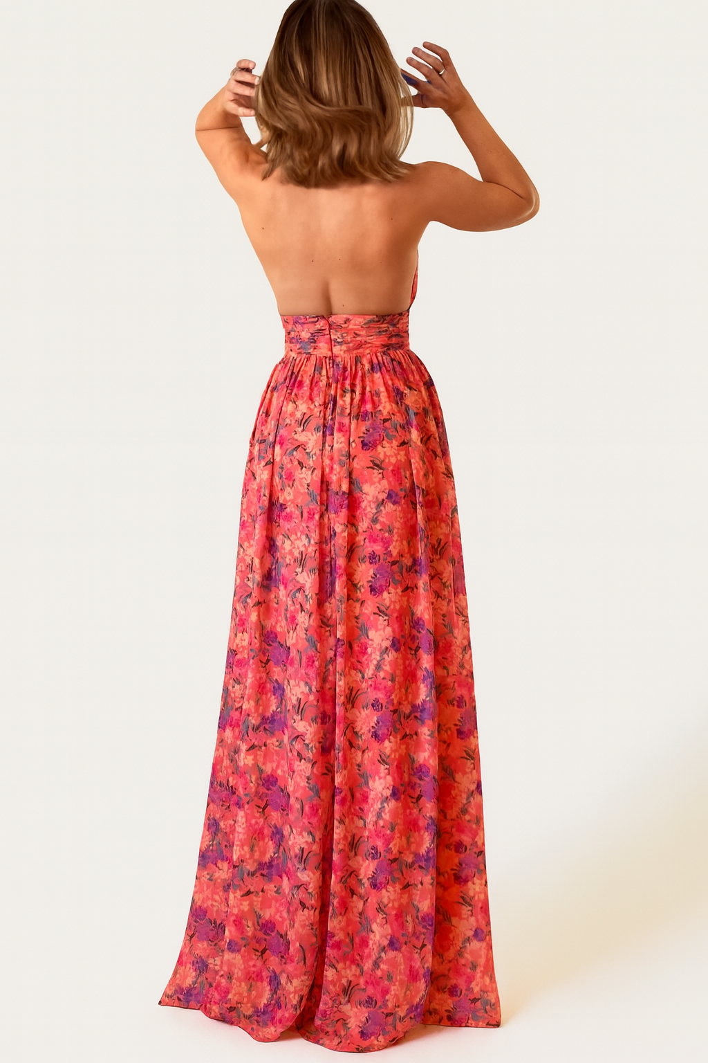 Woman in a red floral open back maxi dress against a plain background.