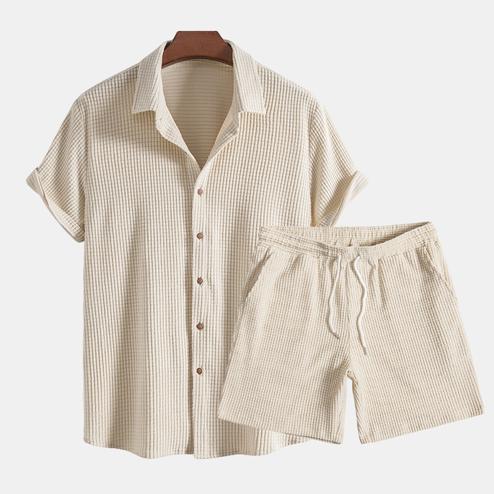 A short sleeve button-up shirt and drawstring shorts set against a plain background.
