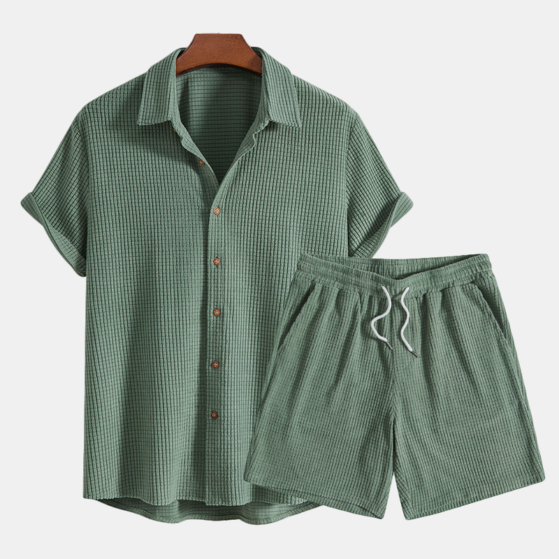 A casual two piece outfit with an open collar shirt and shorts on a plain background.