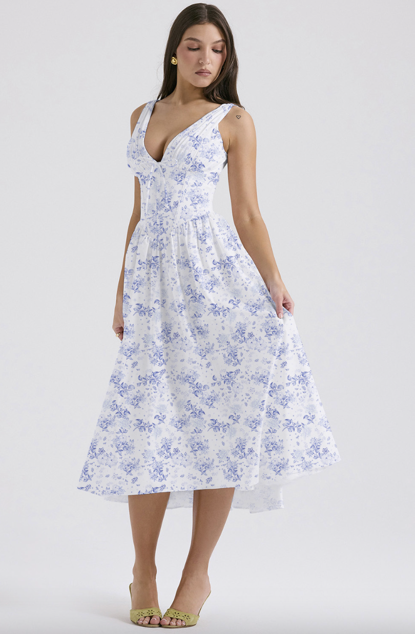 Woman showcasing a feminine warm-weather dress on a plain background.