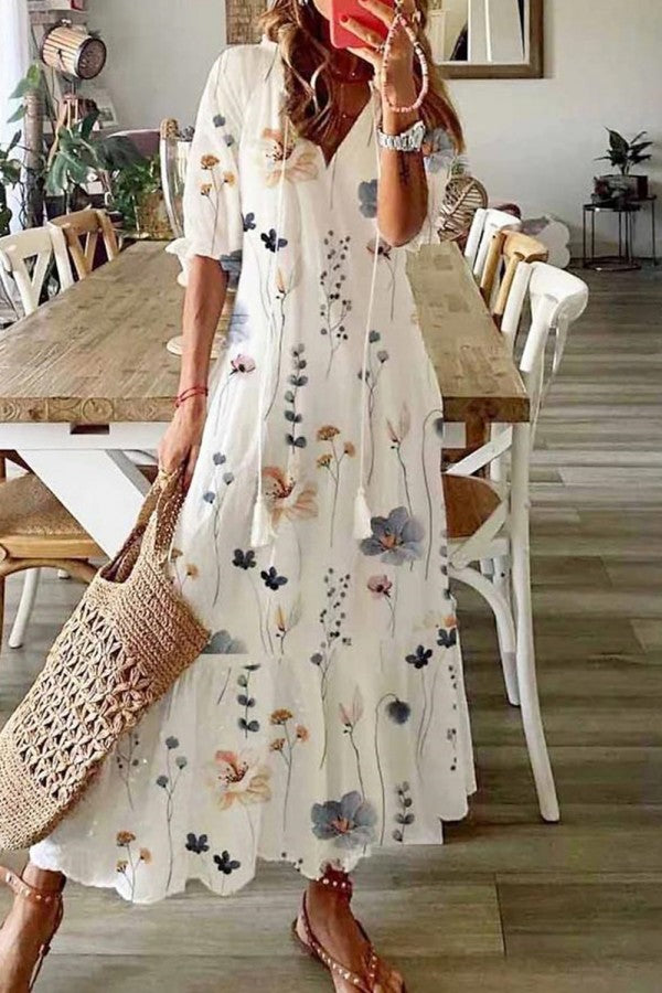 Female model wearing a flowing floral maxi dress with tassel neckline against a plain background.