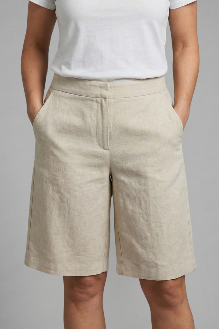 Woman posing in relaxed fit knee length shorts with side pockets on a plain backdrop.