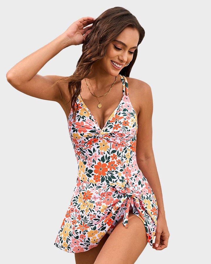 Woman modeling a sleek swim dress with adjustable shoulder straps on a plain background.