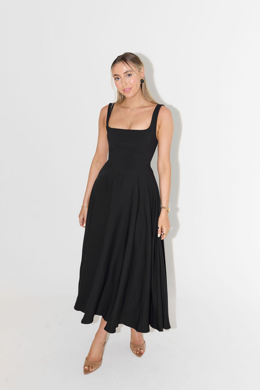 Model wearing a fitted satin midi dress with modern square neckline on a plain background.