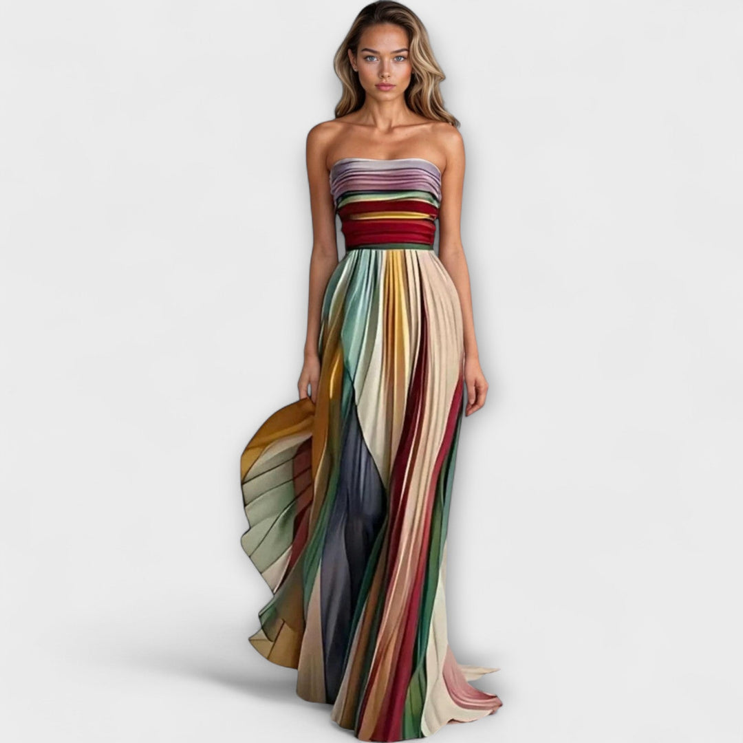 Woman wearing a colorful strapless pleated summer dress on a plain background.