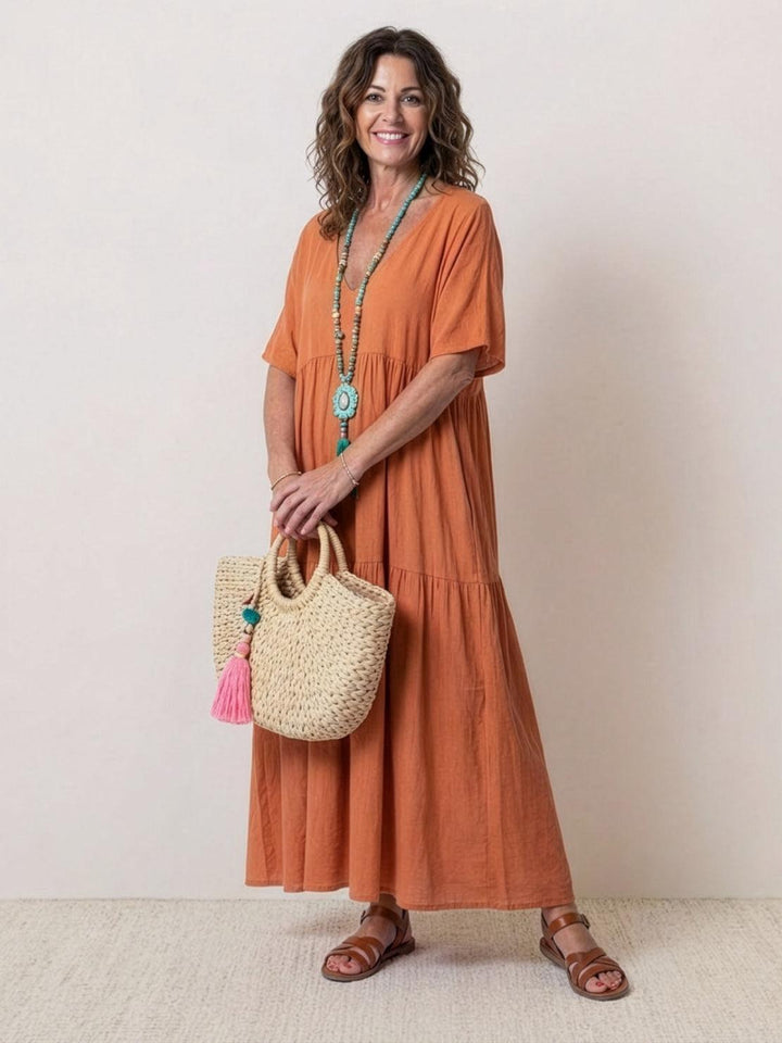 Woman wearing a terracotta tiered maxi dress with short sleeves against a plain background.