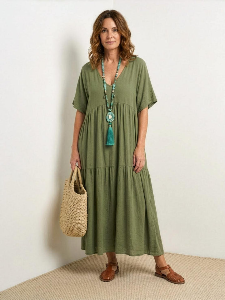 Woman posing in a loose tiered long dress with a relaxed silhouette on a plain backdrop.