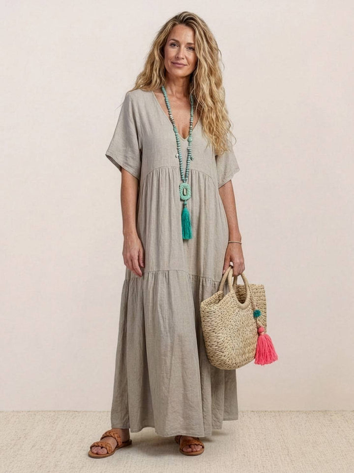 Woman styled in a breezy ankle-length dress with short sleeves on a plain backdrop.
