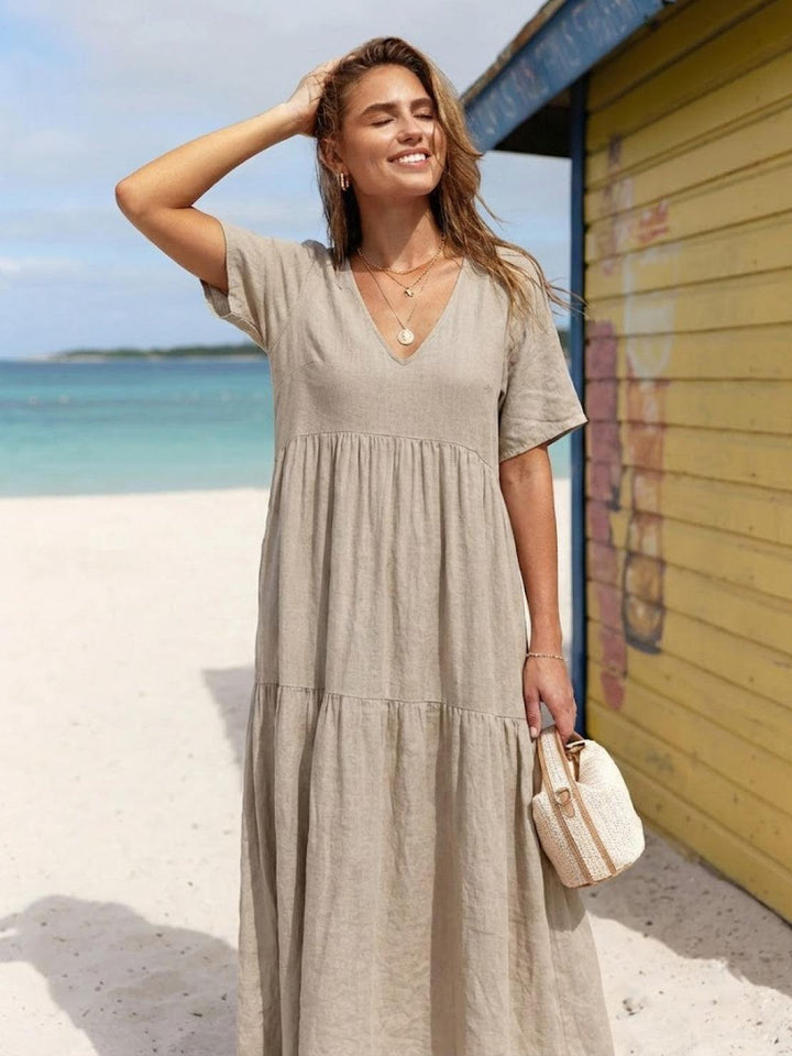 Woman in a flowing terracotta dress with tiered layers and casual styling on a plain background.