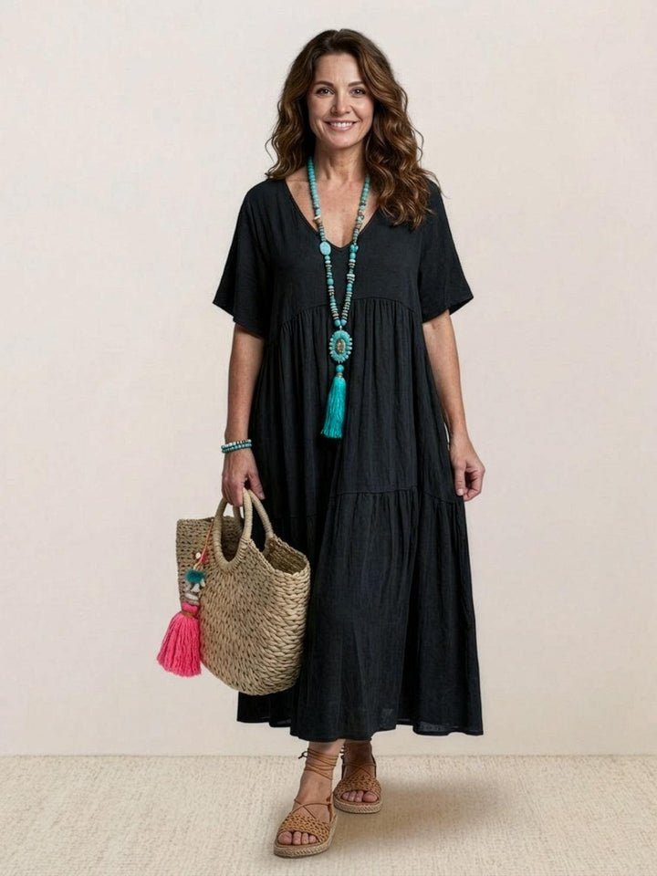 Female wearing a loose maxi dress with soft draping and short sleeves against a plain backdrop.