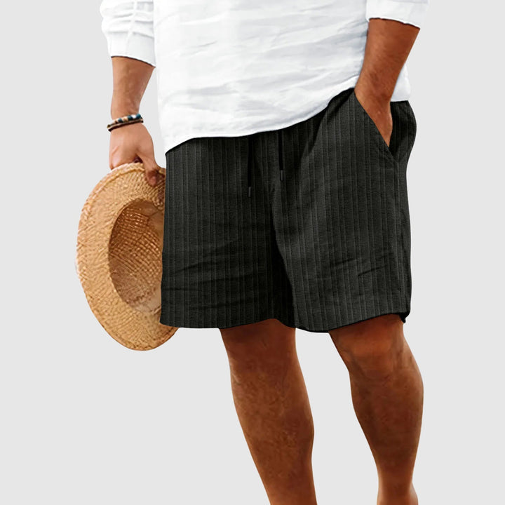 Male model wearing textured drawstring shorts on a plain background.