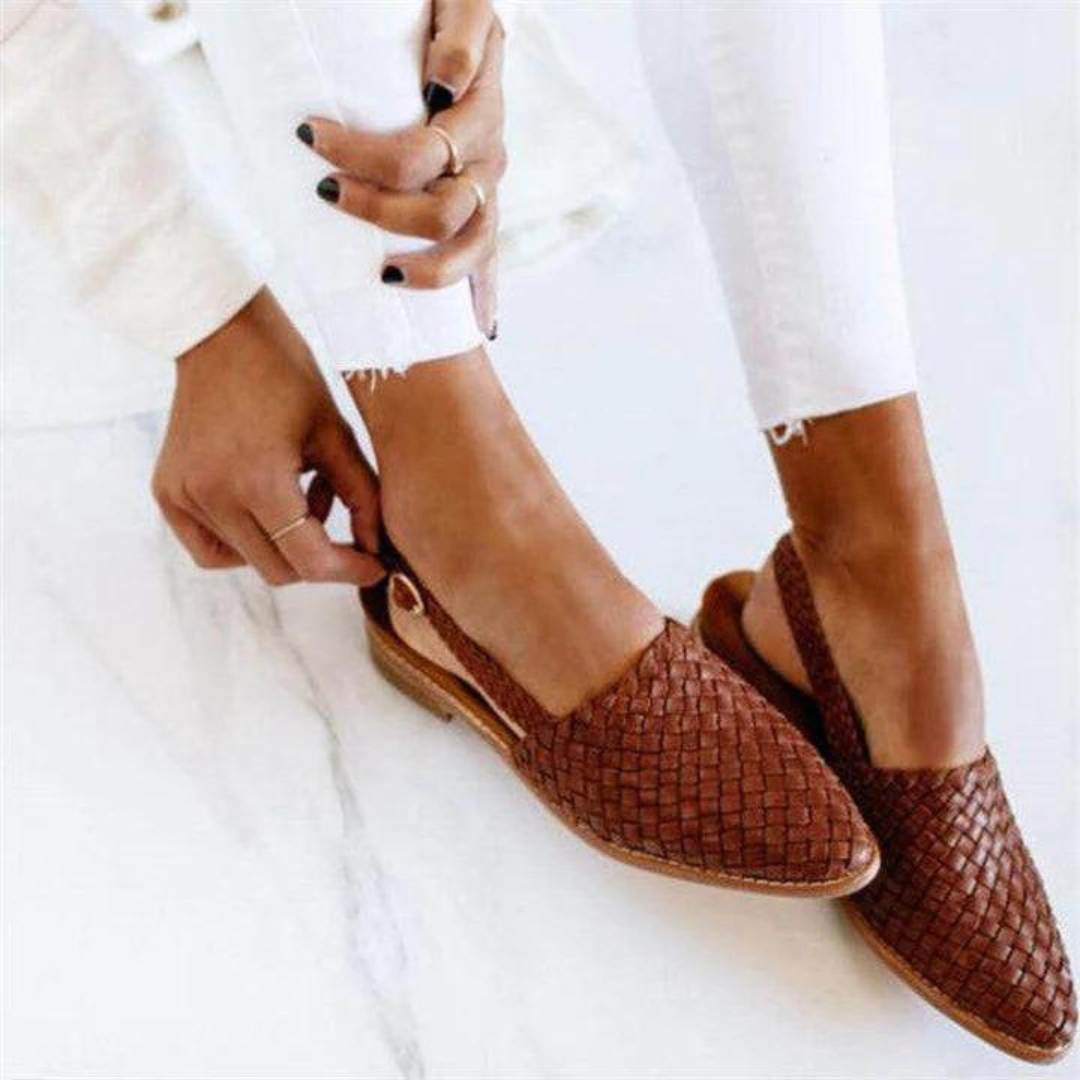 Female wearing woven slip-on flat loafers on a plain background.