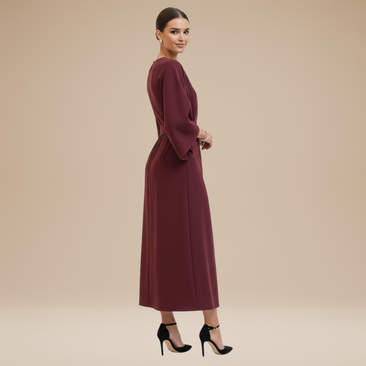 Woman wearing a polished midi dress with wide sleeves and waist tie on a plain background.