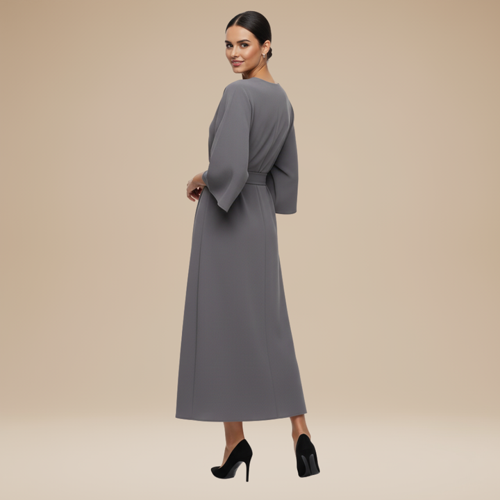 Female model in a graceful belted dress with draped skirt detail on a plain background.