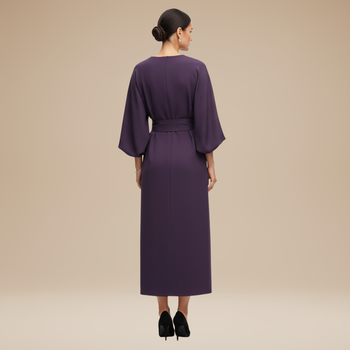 Model wearing a chic belted midi dress with flowing sleeve design on a plain background.