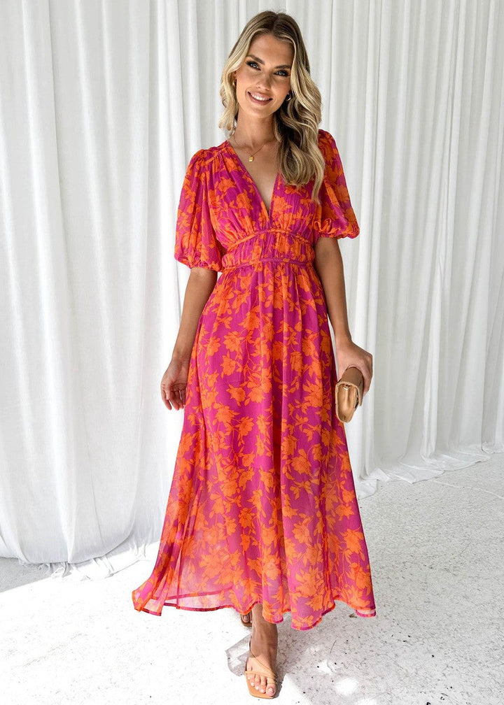 Woman wearing floral maxi dress on plain curtain background, front full view.