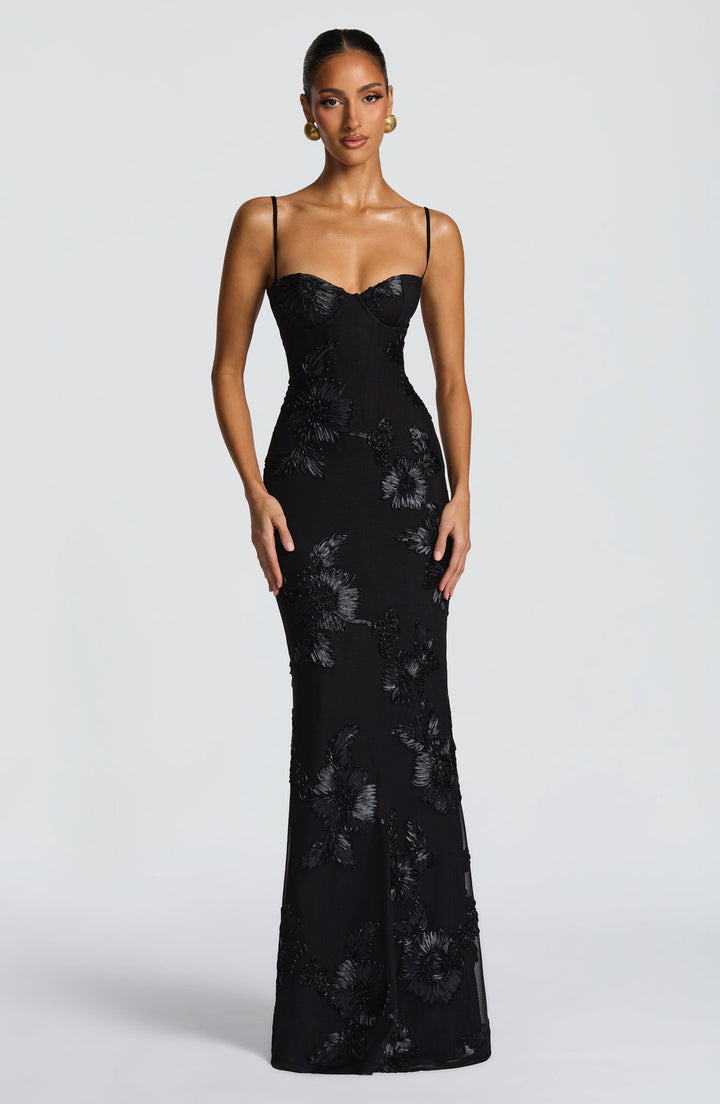Woman in sleeveless embroidered maxi dress studio shot plain background.