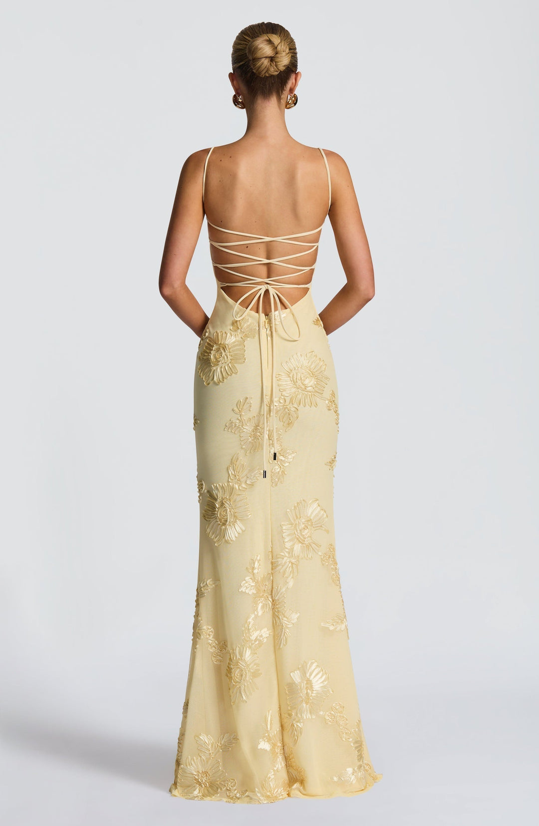 Woman showing fitted embroidered dress full length on plain background, back view