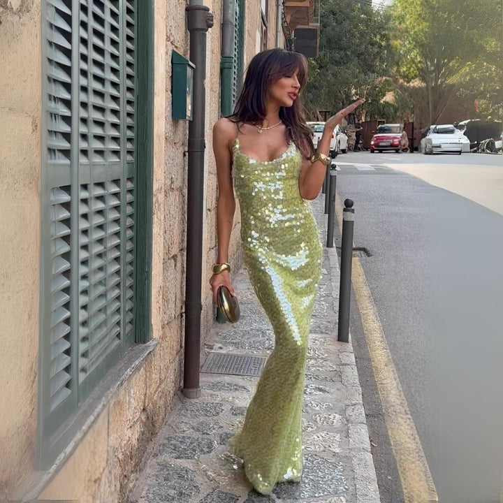 Woman wearing a green sequin maxi dress with spaghetti straps on a sidewalk background.