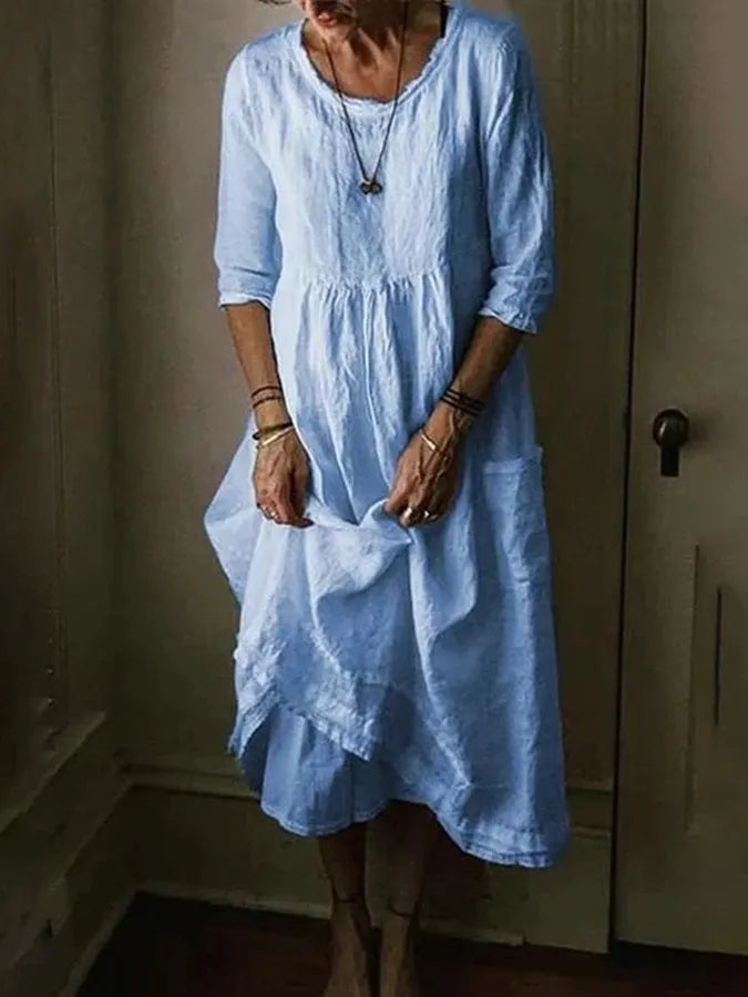 Woman wearing a loose fit midi dress with pockets on a plain background.